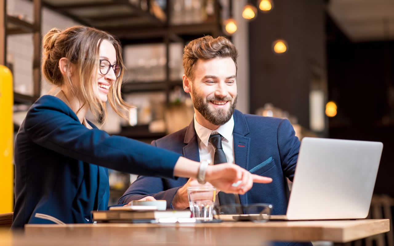 Eine Frau und ein Mann in Business-Kleidung blicken gemeinsam auf einen Laptop.